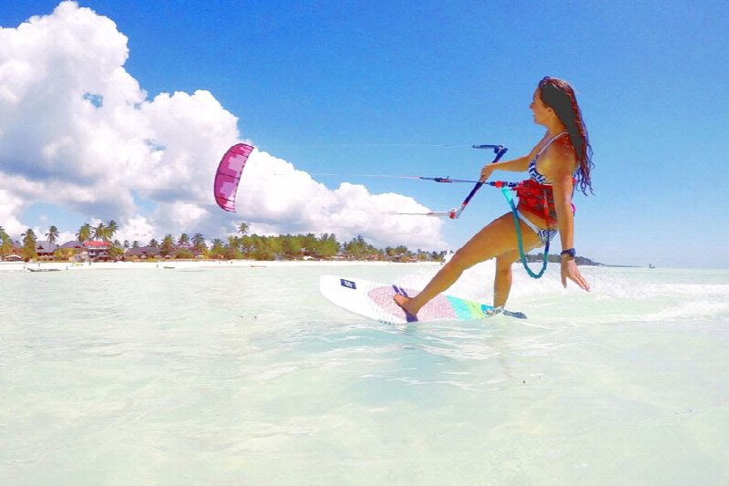 A kitesurfer riding across shallow turquoise water off a Zanzibar beach under a bright sky