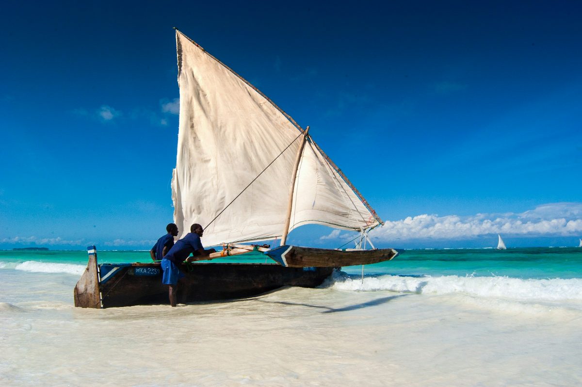 A traditional dhow with its sail up, resting on the sand at the water's edge