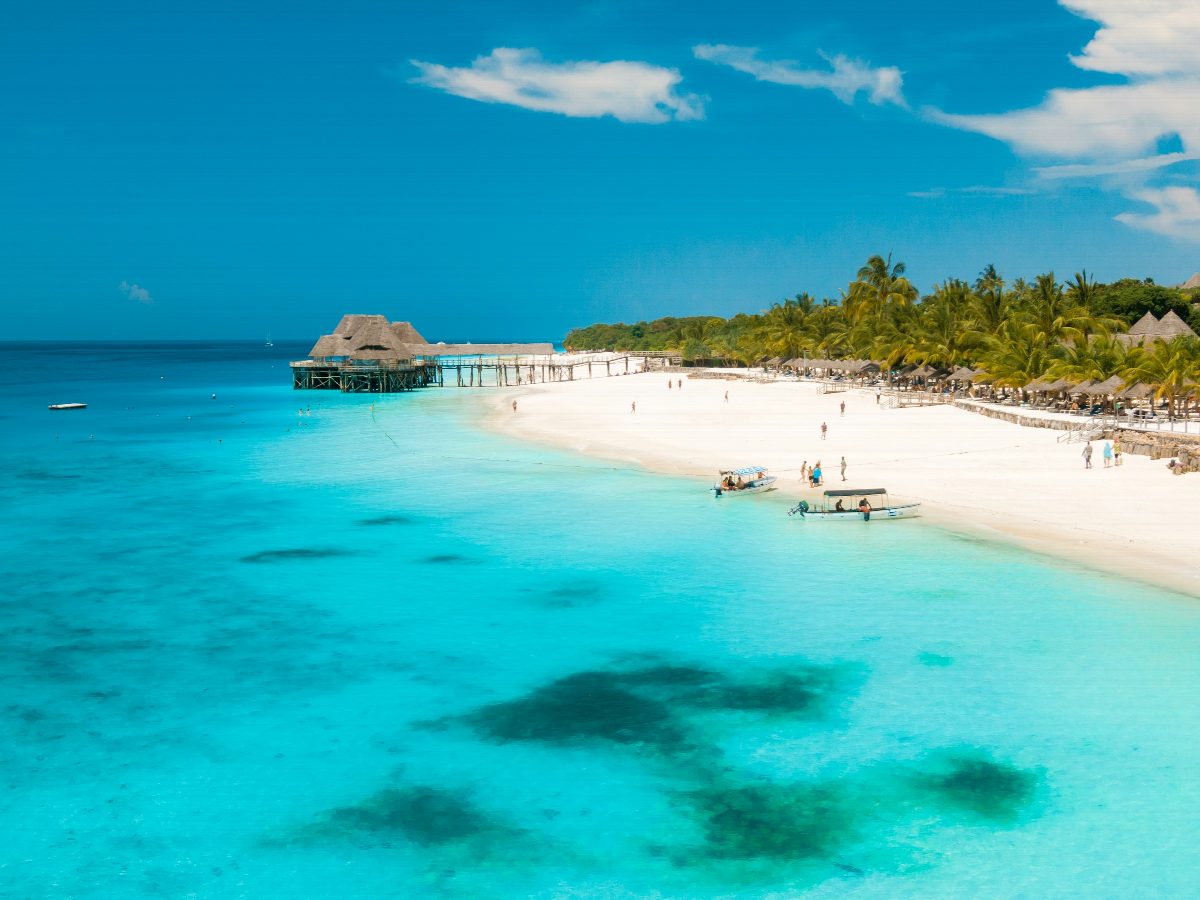 A white sand beach with palms and a wooden pier reaching into clear turquoise water